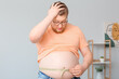 Stressed overweight man with measuring tape at home. Weight loss concept