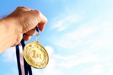 Wall Mural - man hand raised, holding gold medal against sky. award and victory concept