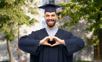 Poster - education, graduation and people concept - happy smiling male graduate student in mortar board and bachelor gown showing hand heart gesture over university campus background