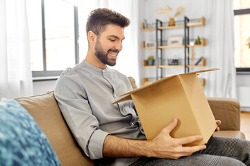 mail delivery, shipment and people concept - happy smiling man opening parcel box at home