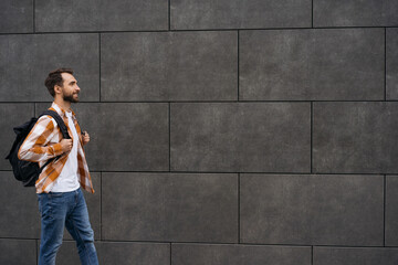 Young bearded man with backpack walking on street, isolated on background. Travel concept