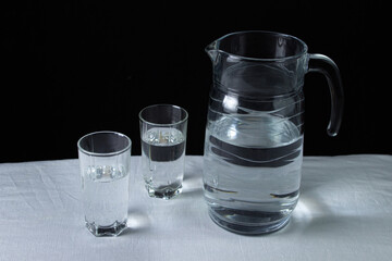 Decanter with water on a black background. A decanter and two glasses filled with water. Clean drinking water. Ecology cleanliness concept.