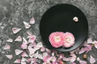 Black plate with ranunculus flowers and petals on grey concrete background. Top view, copy space.