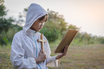 little girl holding bible and crucifix praying to god at sunset background.christian concept