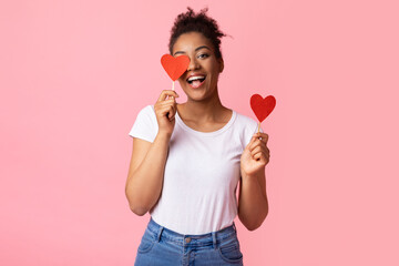 Smiling black woman holding two hearts, covering one eye