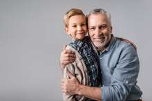 Happy Mature Man Embracing Smiling Grandson While Looking At Camera Isolated On Grey