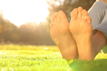 Young woman sitting barefoot on fresh green grass outdoors, closeup