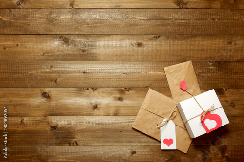 White gift box, gift and envelope wrapped in brown craft paper, tied with twine with bows and labels with red paper hearts on wooden boards. Love, Valentine's, women's day, relations, romantic 
