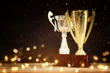 Wall Mural - image of silver and gold trophy over wooden table and dark background, with abstract shiny lights