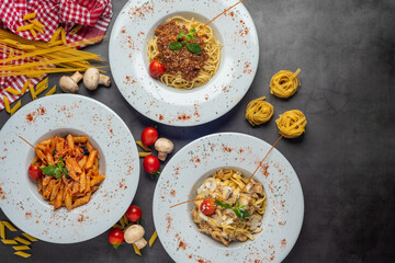 Spaghetti and penne pasta with tomatoes and basil on dark stone table.  Top view.