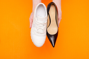 hands hold sneaker and shoe, concept of choice between comfort and business style for woman, orange background