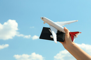 Poster - Woman holding toy airplane and passport against blue sky, closeup