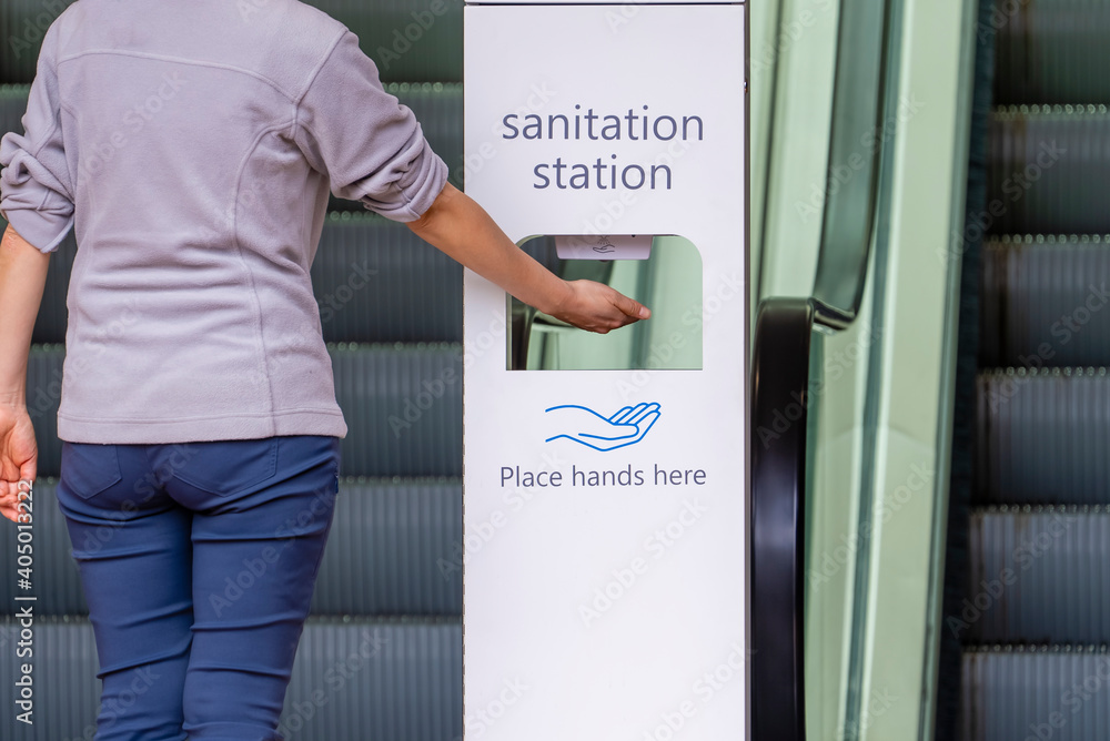 Close-up view of woman sanitizing her hands at sanitation station outside a shopping mall - obrazy, fototapety, plakaty 