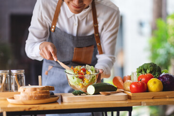 Closeup image of a female chef cooking fresh mixed vegetables salad in kitchen