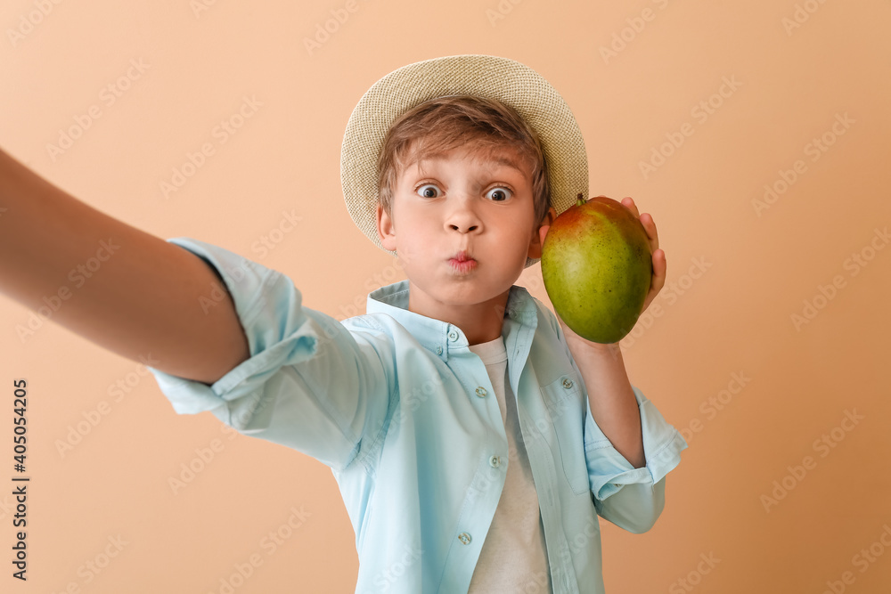 Cute little boy with fresh tasty mango on color background