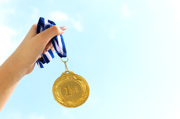 Wall Mural - woman hand raised, holding gold medal against sky. award and victory concept