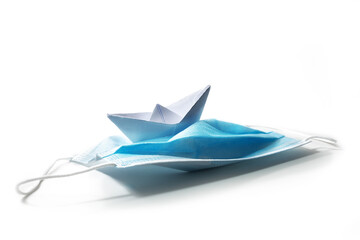 Paper boat keeping course on a surgical face mask against covid-19 pandemic as a ship riding in stormy seas, coronavirus crisis concept, isolated on white, copy space