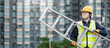 © zephyr_p - Asian maintenance worker man with safety helmet and reflective suit carrying aluminium step ladder at construction site. Civil engineering, Architecture builder and building service concepts