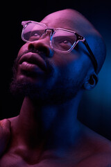 Wall Mural - portrait of a handsome black man in red and blue light on dark background  with glasses on his eyes, he has naked sports torso