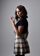 Wall Mural - Close up portrait of pretty brunette woman wearing tartan skirt and blouse.  Posing with gestured hands against a  studio background.