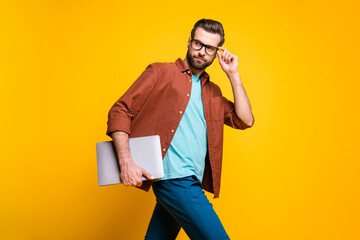 Photo of young handsome man go walk look empty space hold laptop hand touch glasses isolated over yellow color background
