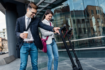 Wall Mural - Two business people with electric scooter talking outside in front of modern business building.