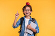 © InsideCreativeHouse - Smart male kid pointing at copy space holding books for school and apple on his head isolated over yellow background