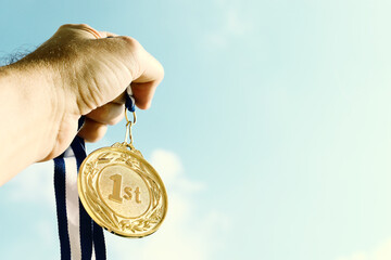 Wall Mural - man hand raised, holding gold medal against sky. award and victory concept