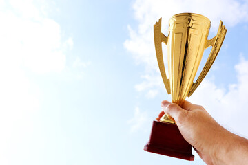 Wall Mural - man holding up a trophy cup as a winner against the blue sky. award and victory concept