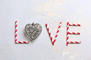 Saint Valentine day greeting card, word LOVE made from striped red and white straws and silver metallic heart on grey