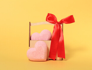 Two pink hearts and wooden box with red ribbon bow on yellow background.