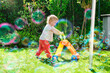 © Nektarstock - Child Pushing Toy in Sunny Backyard with Soap Bubbles