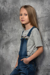 Canvas Print - girl child in a gray t-shirt and denim overalls on the background of an old wall