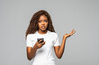 © F8  \ Suport Ukraine - Portrait of confused puzzled woman with afro hairstyle wearing t-shirt holding cell phone and expressing misunderstanding over white background