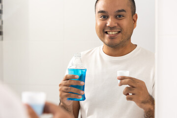 Wall Mural - Young man is gargling with a blue mouthwash. For good dental health and fresh bad breath