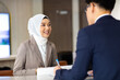© NVB Stocker - Portrait of muslim woman receptionist at desk in lobby.  Asian business man standing at reception desk and talking to muslim woman receptionist.