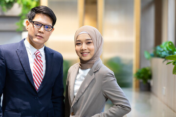 Wall Mural - Portrait of young Asian muslim woman wearing hijab head scarf and Asian business man in suite in moder office.