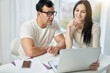 © Friends Stock - Benefits of online courses. Happy hispanic couple, man and woman making video call, talking on webcam while contacting client remotely, using laptop at home