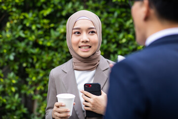 Wall Mural - Young business muslim woman and business man colleague walking and discussing outside the office. Woman is holding a coffee and businessman is holding a digital tablet outdoor.