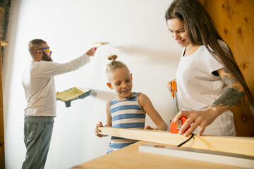 Young couple, family doing apartment repair together themselves. Mother, father and son doing home makeover or renovation. Concept of relations, moving, love. Measuring, painting with roller