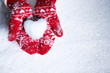 Female hands in knitted mittens with snowy heart against snow background