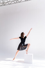 Canvas Print - A slender girl in a black sports dress poses while dancing on a white isolated background. Girl athlete dancing on a white isolated background with place for text or logo.