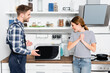 © LIGHTFIELD STUDIOS - cheerful young woman with clenched hands looking at fixed microwave near handyman in kitchen