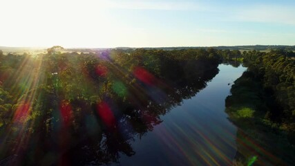 Wall Mural - Slow descend over river facing the sun with lens flare at sunset in Australia