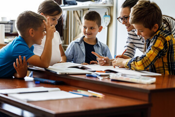 Female teacher helps school kids to finish they lesson.They sitting all together at one desk.