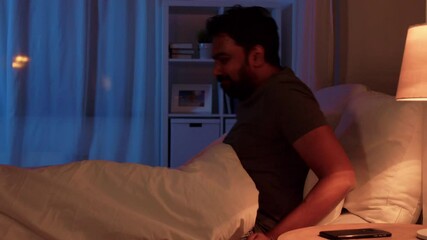 technology, internet, communication and people concept - young indian man with smartphone lying in bed at home at night