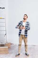 Wall Mural - full length of young man with saucepan looking up while standing near cardboard boxes and ladder under leaking ceiling at home