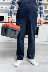 Wall Mural - cropped view of young handyman holding toolbox with blurred kitchen on background