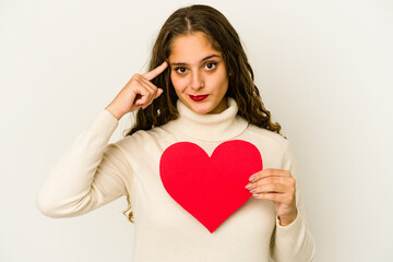 Young caucasian woman holding a heart valentines day shape isolated pointing temple with finger, thinking, focused on a task.