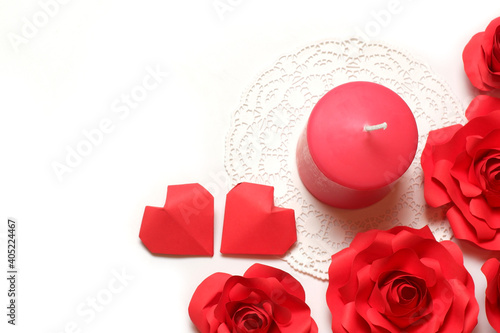 Thick pink aromatic candle on white openwork paper napkin, couple 3D handmade paper hearts and few roses on white background top closeup view isolated. Love, rendezvous, relations, dating concept 